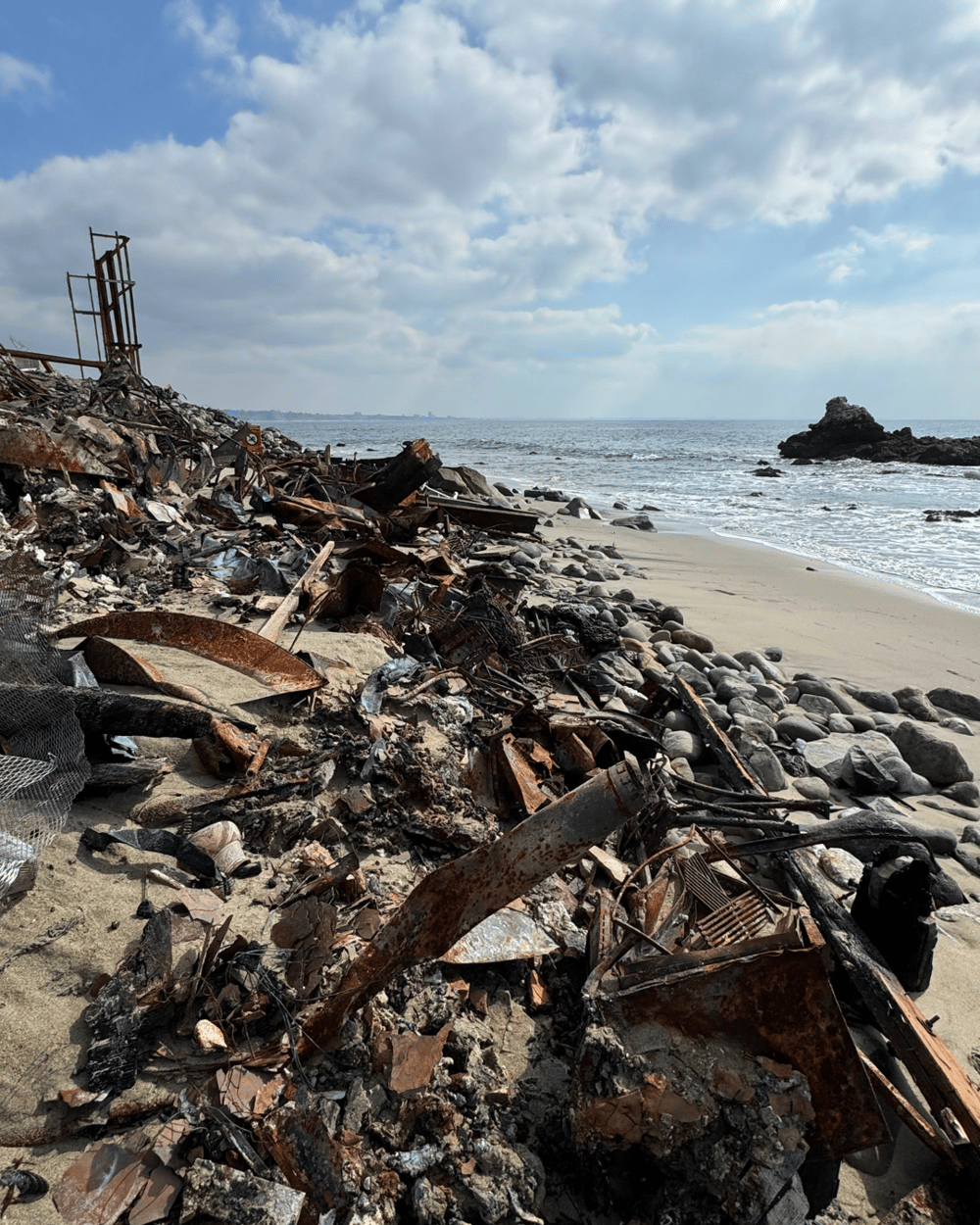 Debris from waterfront houses line the sand and shoreline of beach.