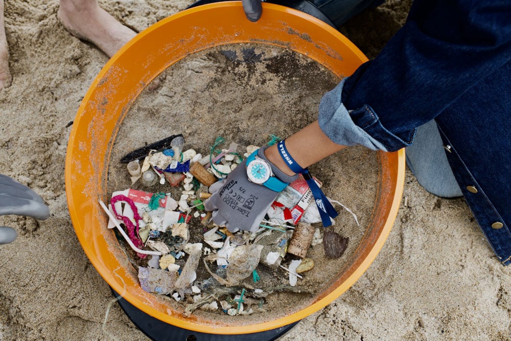Picking up trash at a beach cleanup wearing a Breitling watch.