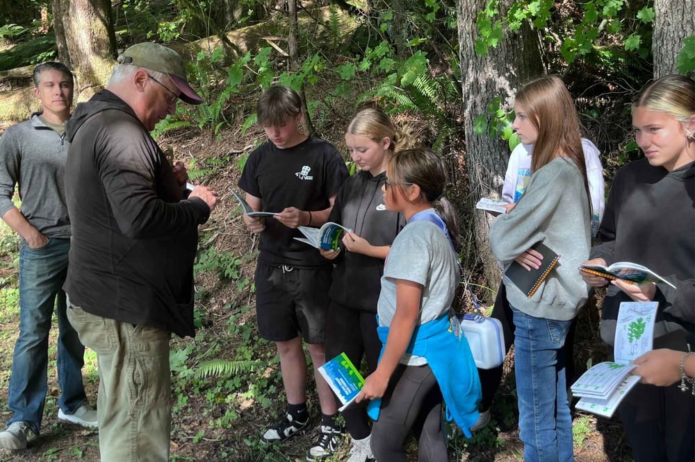 Bruce stands with a group of students in nature surrounded by threes.