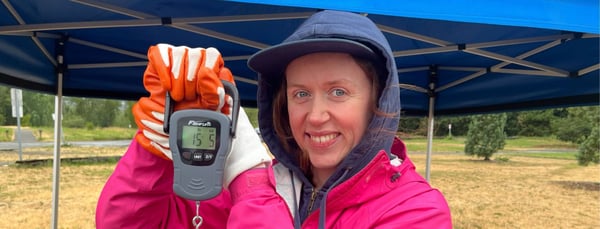 Diana holds a scale with trash that reads 15 pounds, 5 ounces.