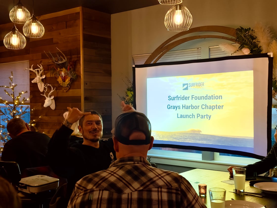 A stoked volunteer throws up a shaka in front of the Grays Harbor Launch Party slide