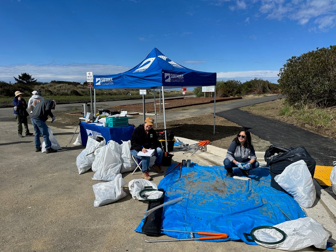 Volunteers sit in front of a tarp, surrounded by plastic bags full of beach trash waiting to be sorted, counted, and entered into our database