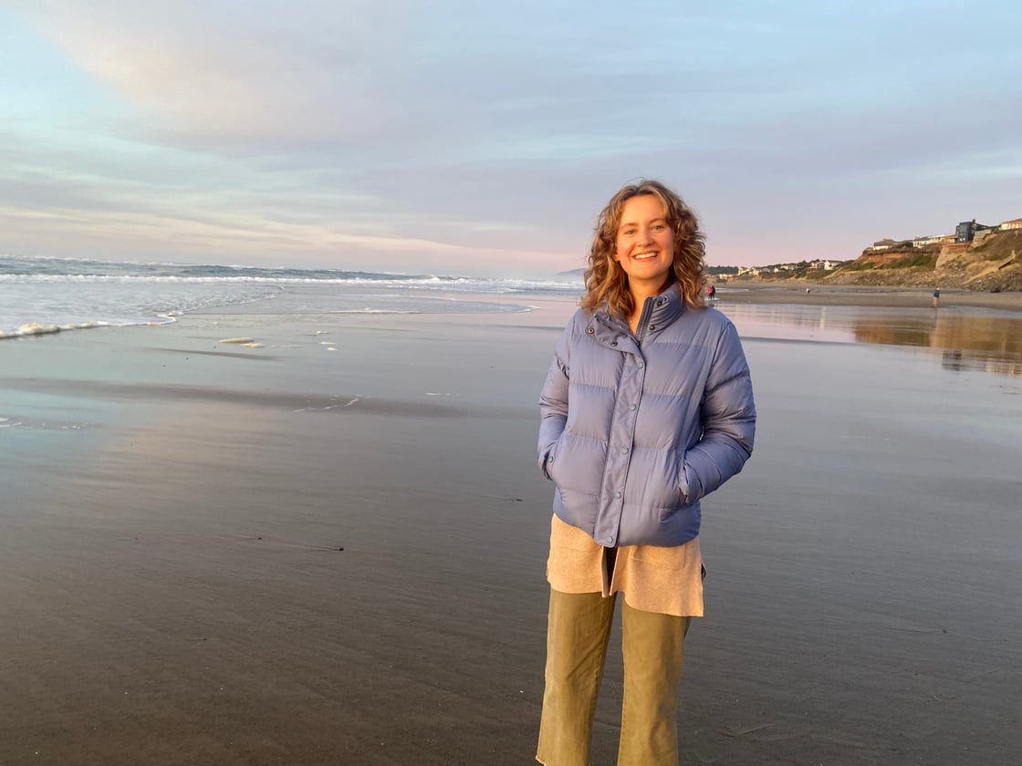 Taylor Wood stands on a beach, smiling at the camera