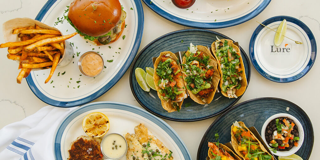 Shot from above: burger and fries, fish tacos, crab cakes.