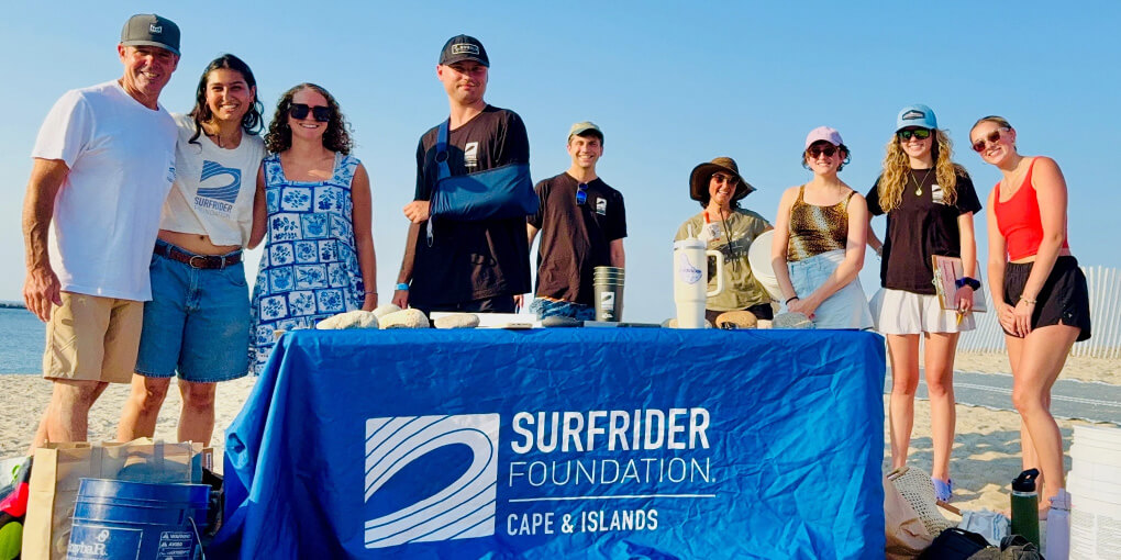 Surfrider volunteers pose at a table with a blue Surfrider tablecloth that reads, "Surfrider Foundation Cape & Islands."