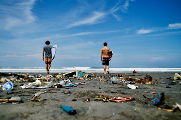 Two surfers on a beach full of plastic trash