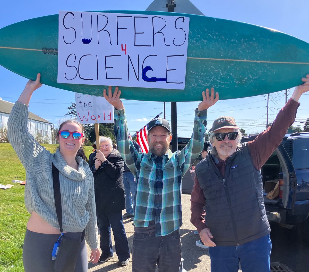 A photo of Oregon volunteers at a protest with a sign on a surfboard supporting science