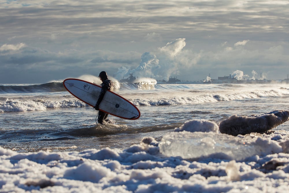 A surfer walks out to sea surrounded by icy shores.