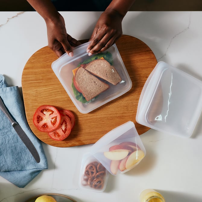 Stasher bags of different sizes with a sandwhich, apples and pretzels inside.