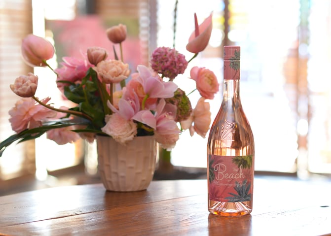 A bottle of The Beach rosé in front of a bouquet of pink flowers