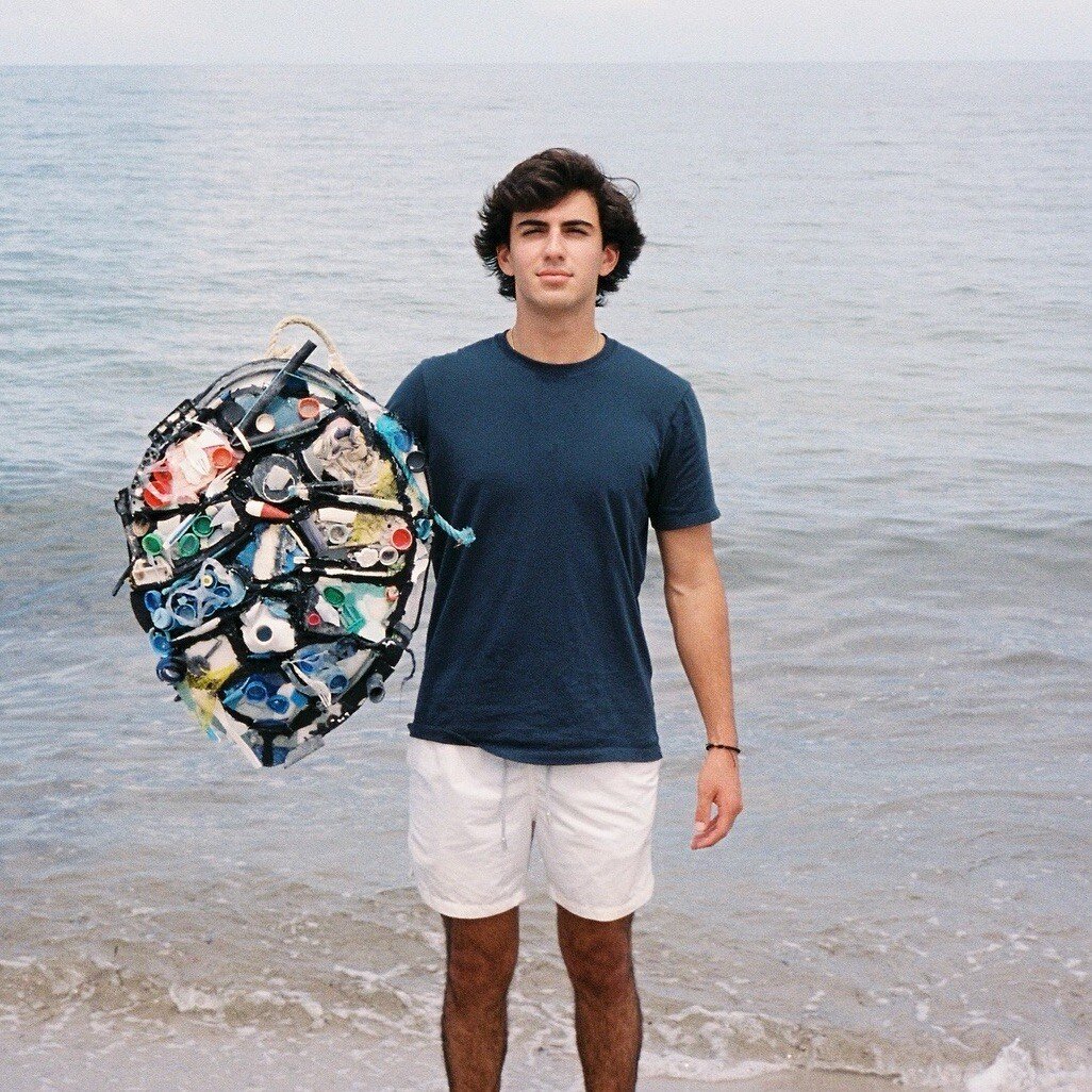 Young man holding a sea turtle shell made out of colorful pieces of trash.