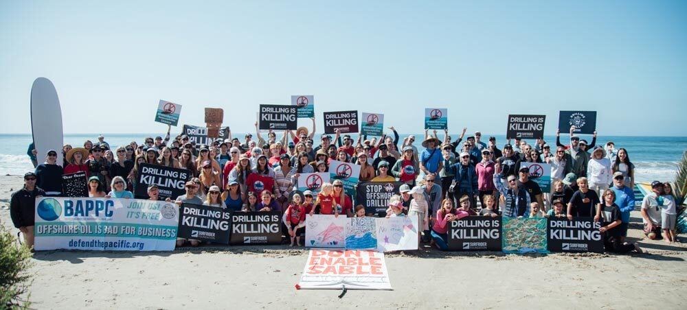 Volunteers hold protest signs at the Paddle Out to Protect Our Coast event at Refugio Beach in California