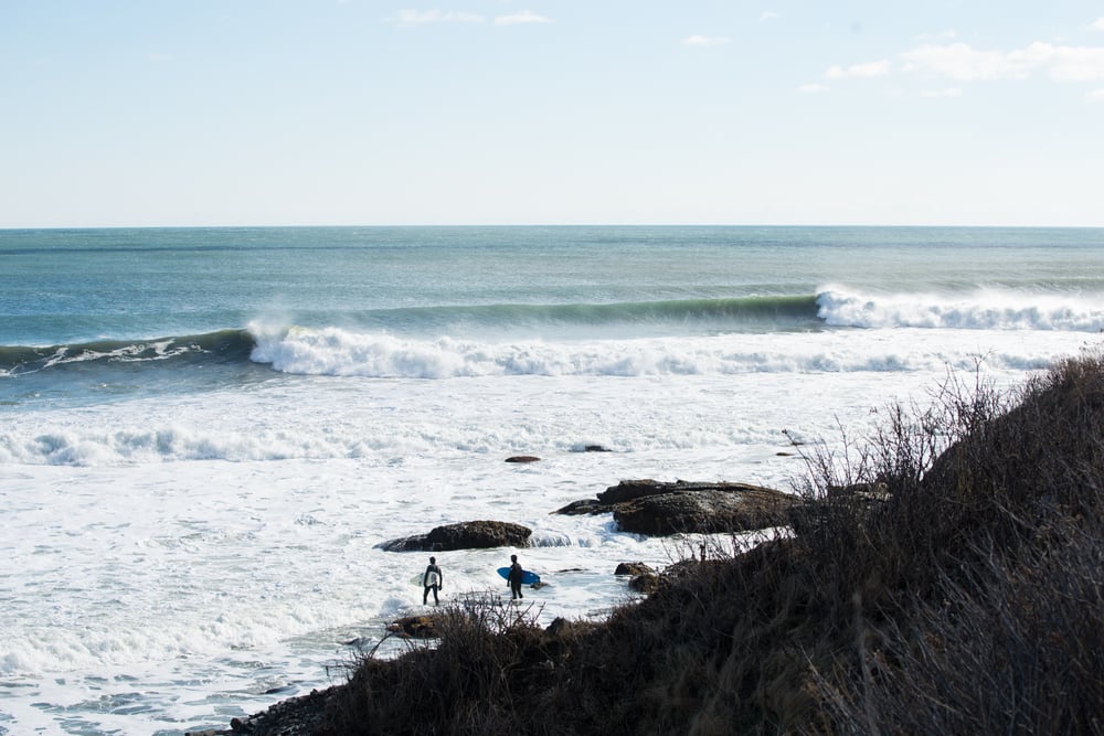Two surfers walk out into the water between sets.