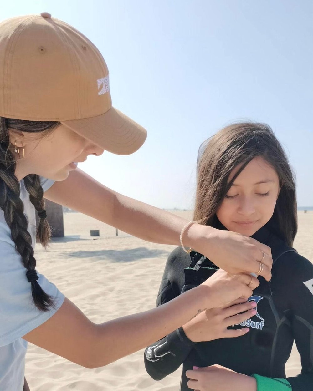 Tatiana helps a young surfer putting on a wetsuit.