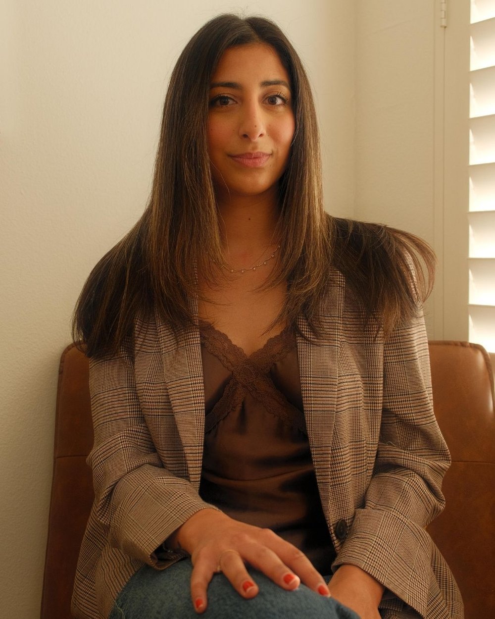 Tatiana sitting in a brown leather chair, wearing a brown blouse and a plaid blazer.