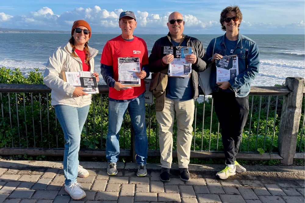 Tico poses with volunteers after collecting Drilling is Killing postcard petitions.