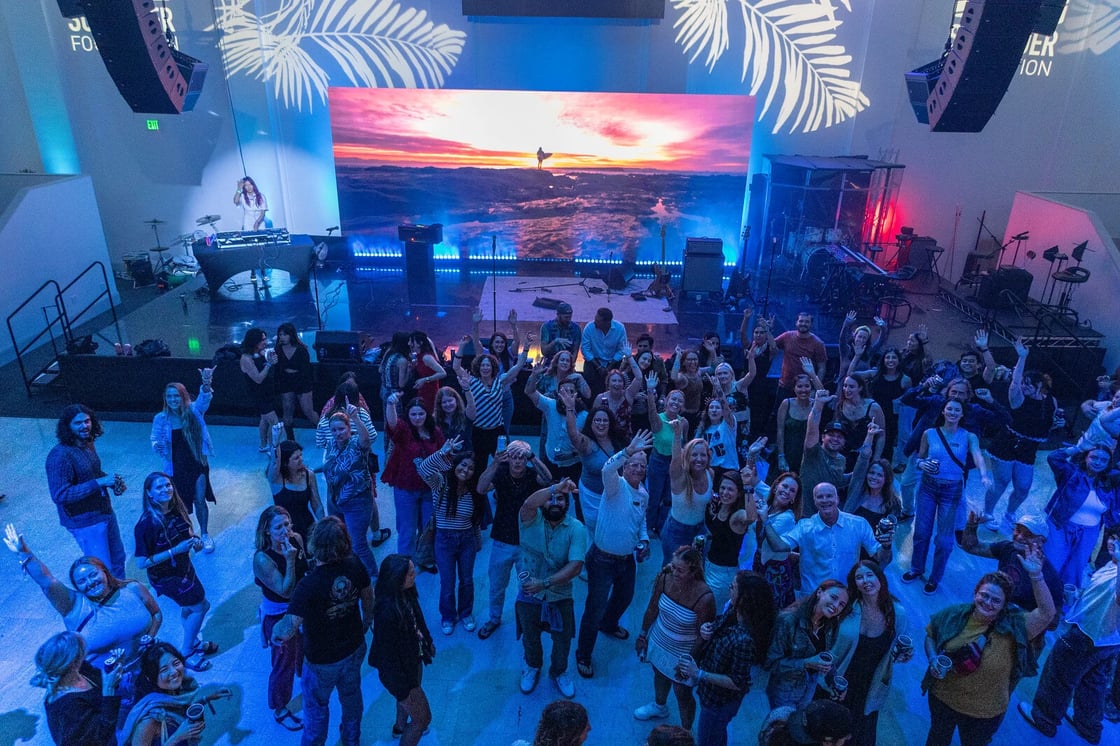 Ariel view of the post-conference party - people are gathered in front of a screen showing a sunset with blue lighting