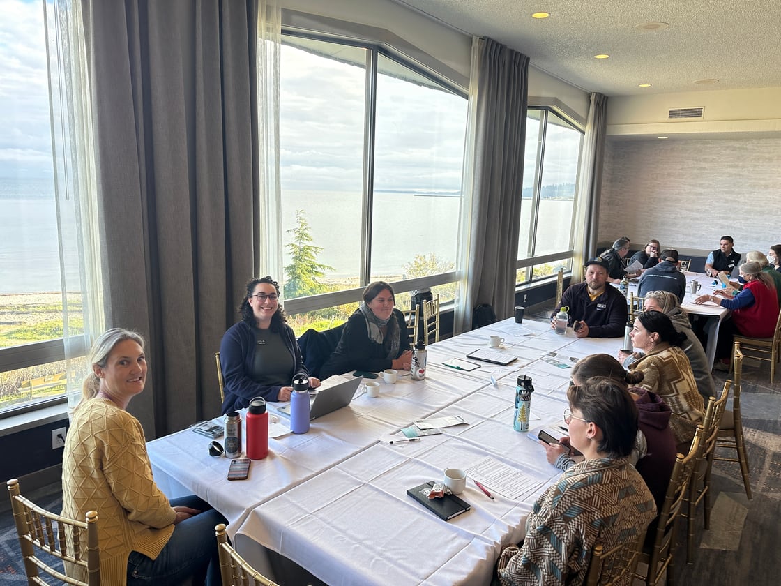 Folks sitting around a table with a view of the Port Angeles waterfront