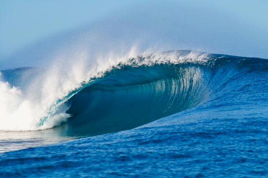 A bright blue wave breaks under a clear sky; 📸: Morgan Maassen 