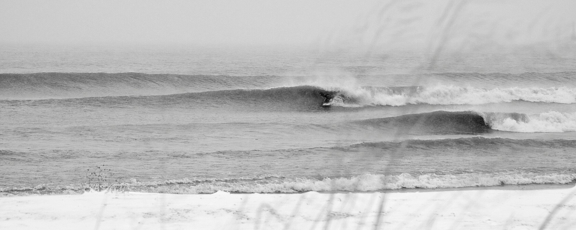 Black and white image of peeling righthand wave with a surfer tucked into a small barrel.
