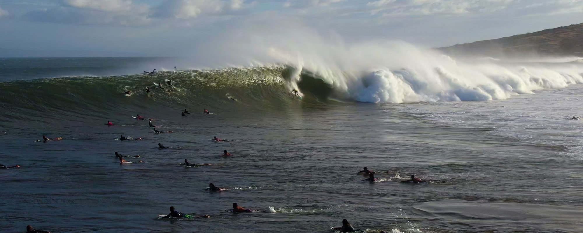 A dozen surfers at Mā'alaea paddling to make it over a wave with one surfer dropping in.