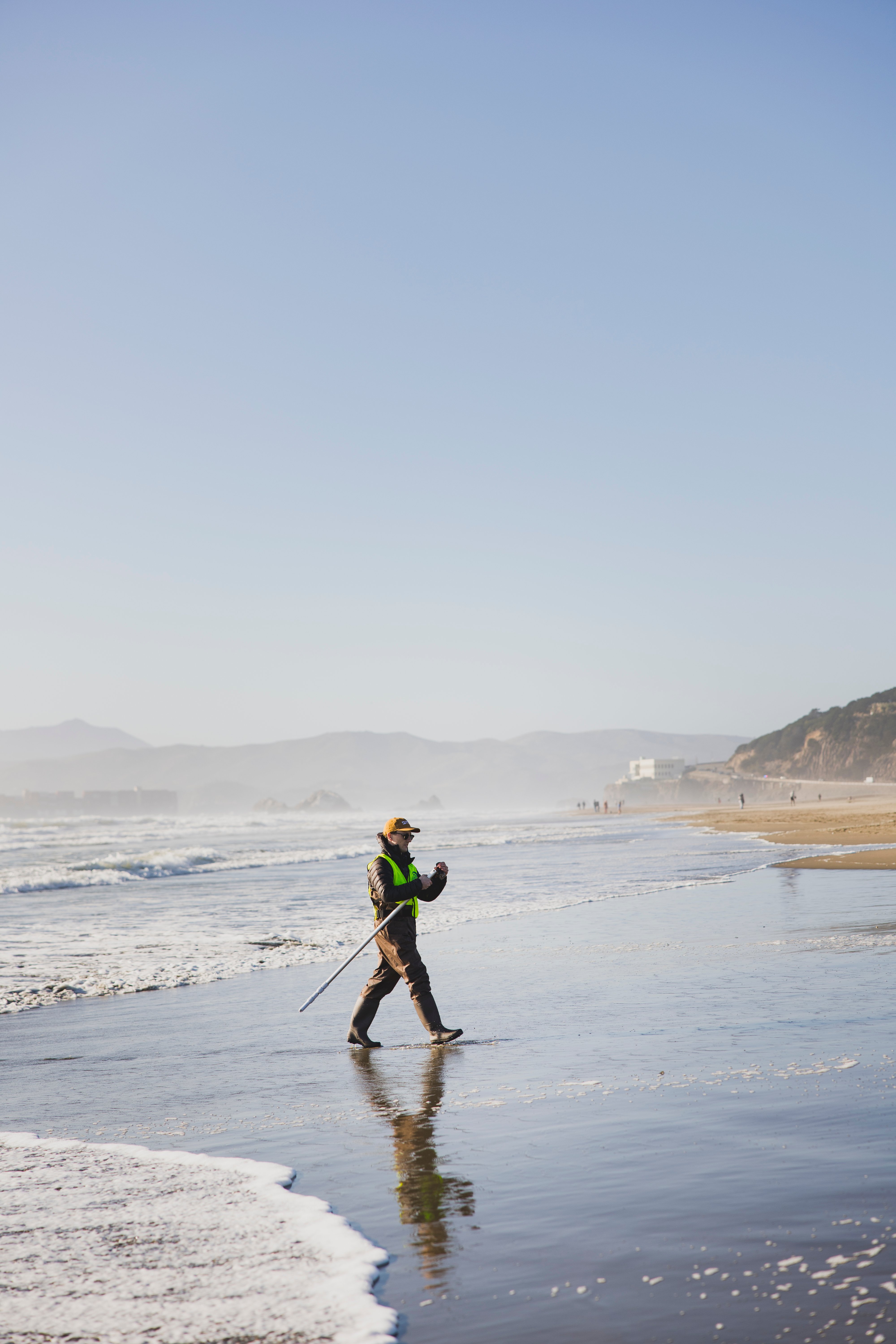 Kyle testing water at Ocean Beach, San Francisco, wearing waders and a hi-viz vest.