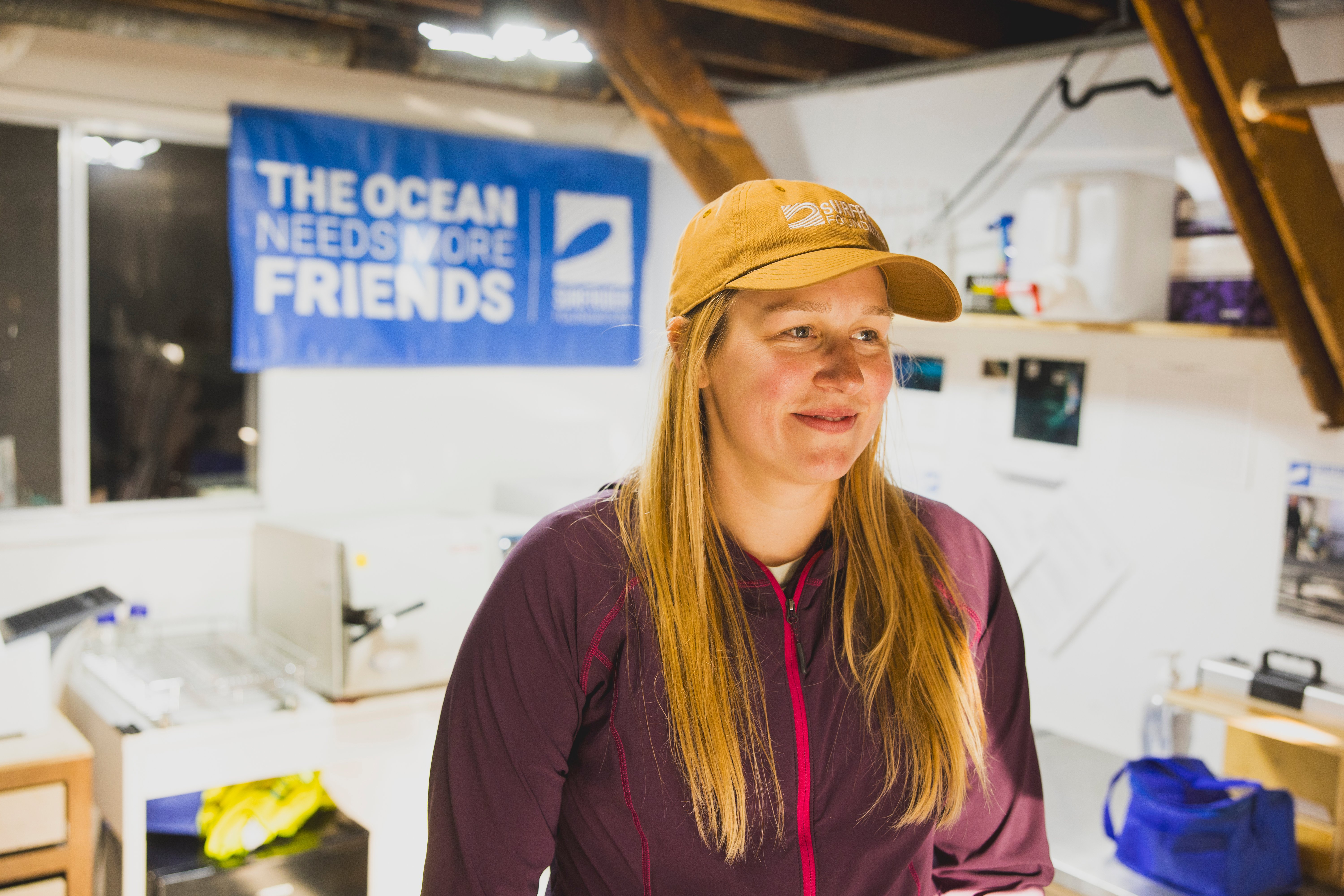 Amanda in her garage, which doubles as a blue water task force lab. she's wearing a light brown surfrider hat with a maroon windbreaker on.