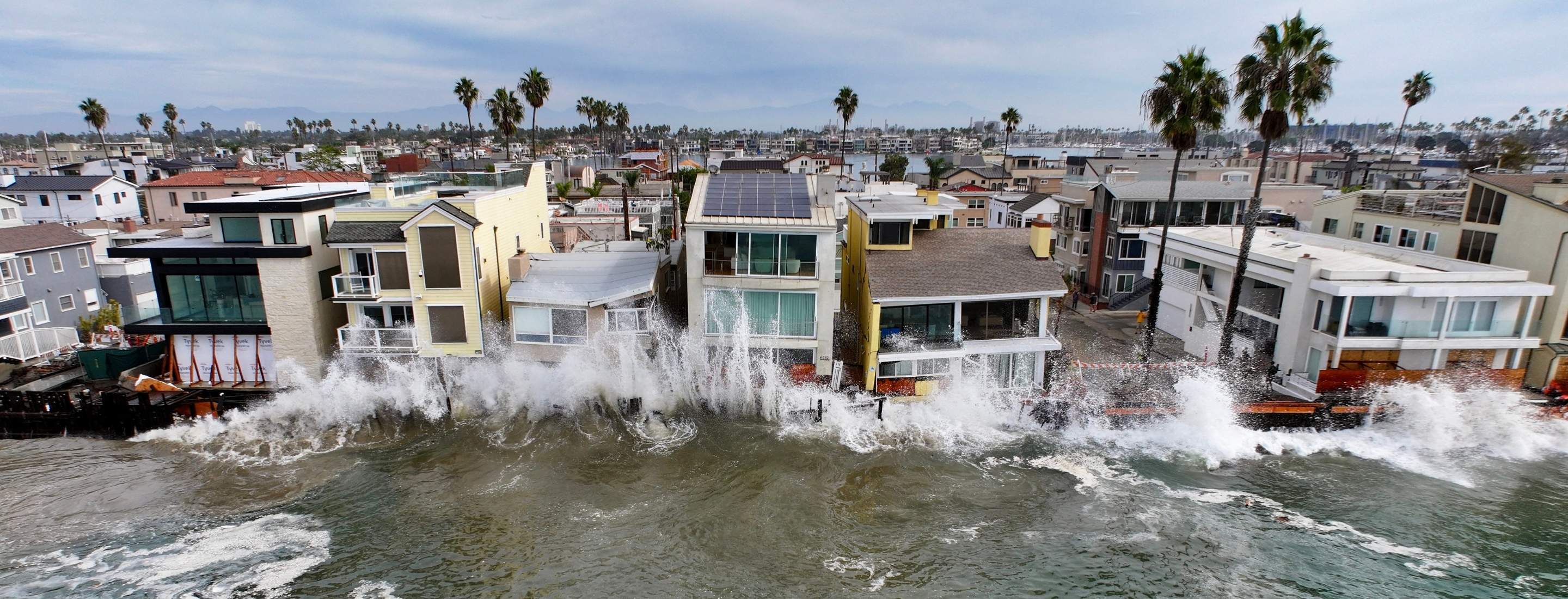 A wave hits houses in Long Beach, CA