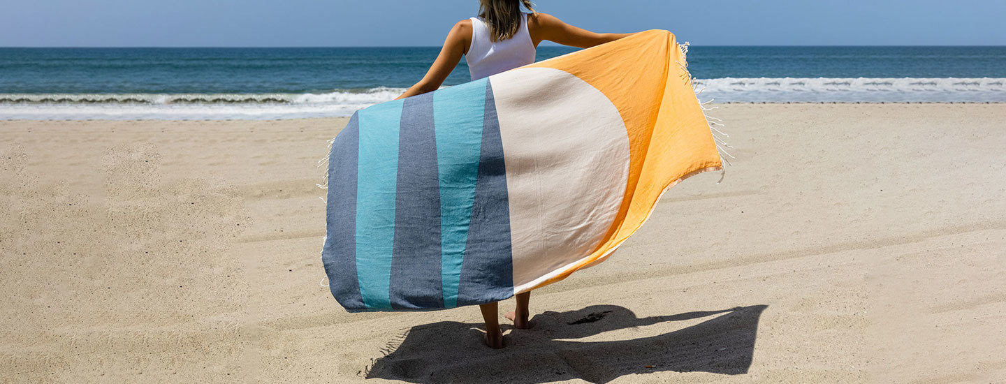 Person holding a Sand Cloud towel behind them on the beach.