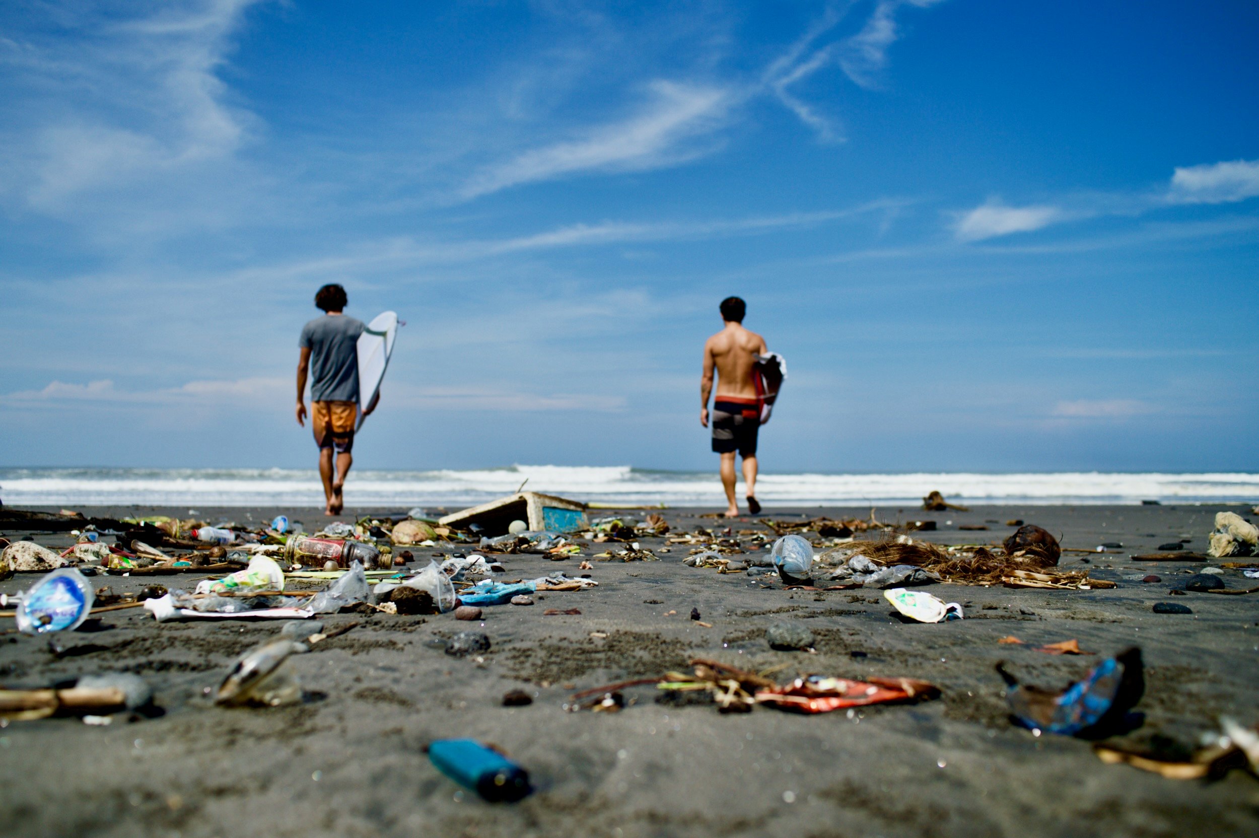 Two surfers on a beach full of plastic trash