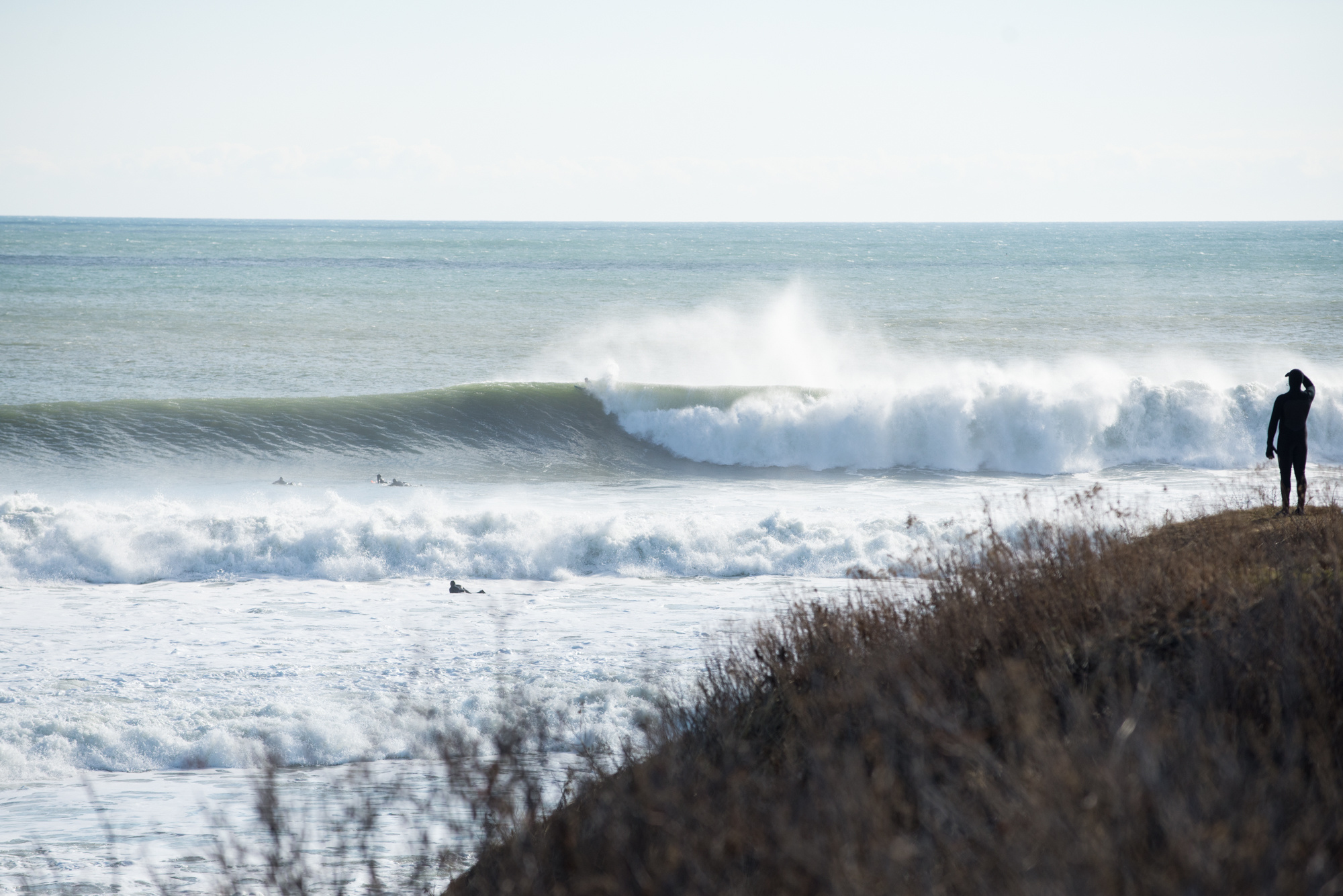Surfer in foreground while large, righthand wave peels in background