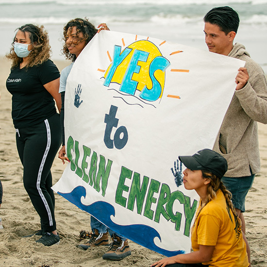 People on beach carrying sign that says Yes To Clean Energy.
